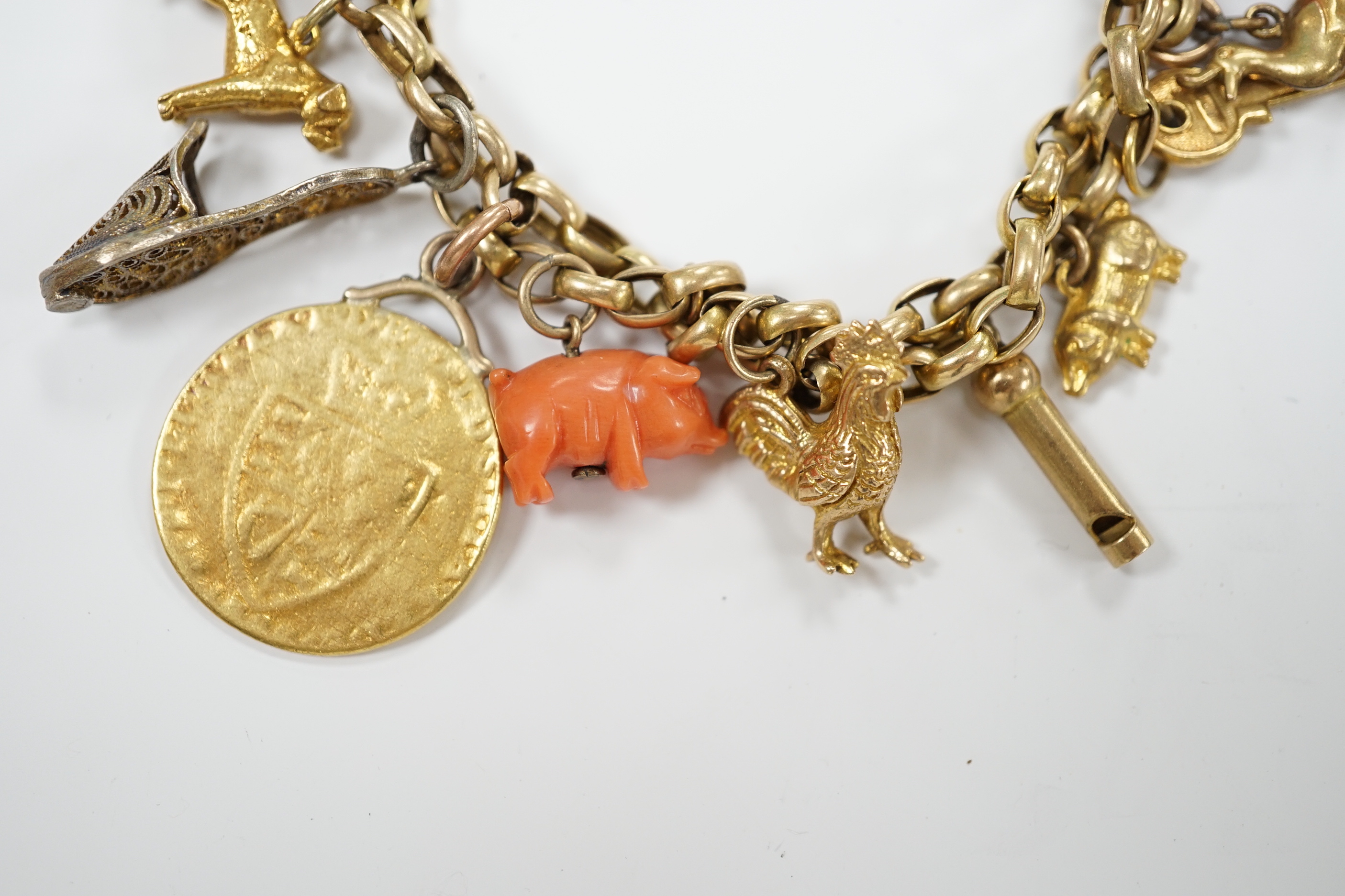 An early 20th century 9ct multi link charm bracelet, hung with sixteen assorted charms, including 9ct, coral, enamelled and a worn spade guinea